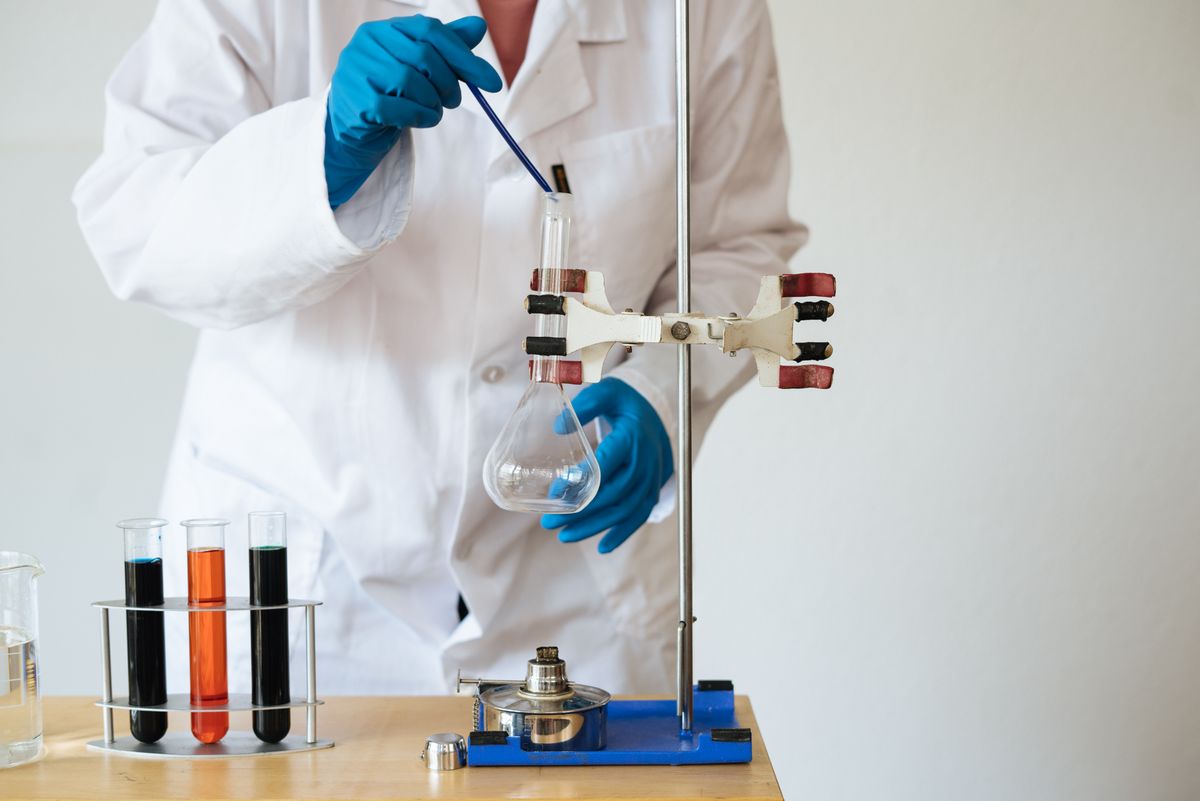 Lab technician in blue gloves conducting analysis with a flask and labeled test tubes